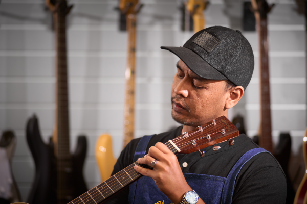 Guitar technician in Malaysia checking guitar neck alignment during service.