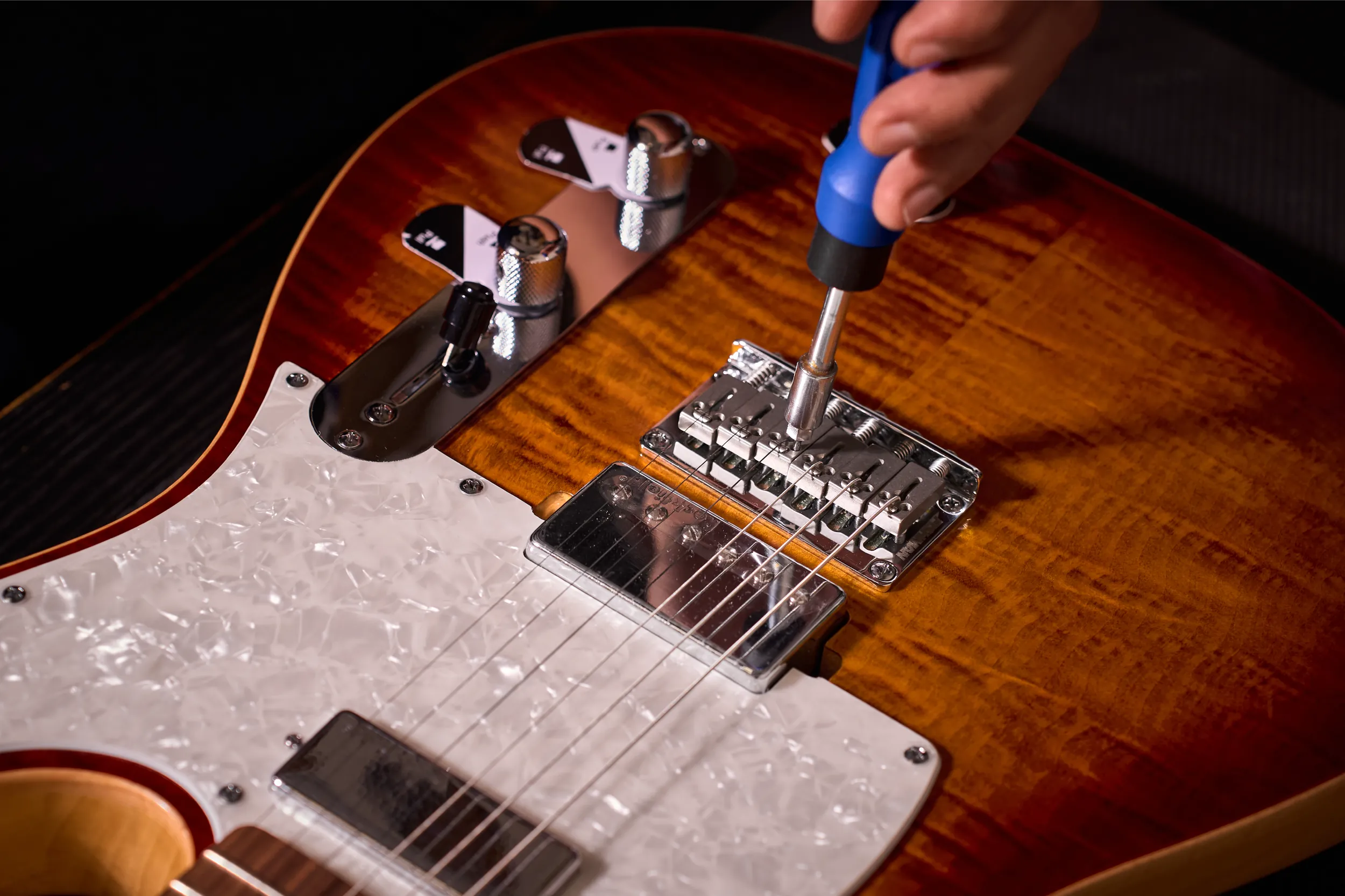 Close-up of technician adjusting guitar saddle height during service in Malaysia.
